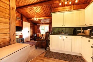 A cozy cabin interior with wooden walls, a dining area, a kitchen with white cabinets, and a fireplace.