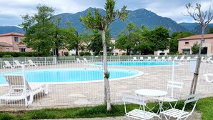 A pool area with white chairs and tables, surrounded by a fence, with mountains in the background.