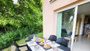 An outdoor dining area with a table set for four, surrounded by chairs, and a kitchen visible through an open door.
