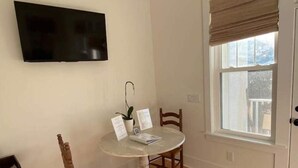 Un pequeño comedor con una mesa redonda, dos sillas, una planta en maceta y un televisor montado en la pared.