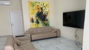 Een woonkamer met een beige bank, een salontafel, een televisie en een schilderij aan de muur.