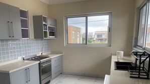 Een moderne keuken met grijze kastjes, een roestvrijstalen fornuis en een raam met uitzicht op gebouwen.