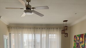 Een ruime woonkamer met een beige bank, een eethoek met een glazen tafel, en een plafondventilator.