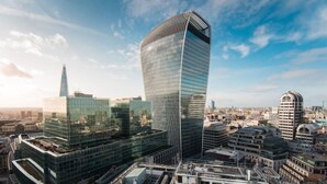 A modern skyscraper with a curved glass facade, surrounded by other high-rise buildings in an urban setting. - Contemporary flat in the City (London)