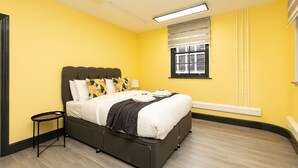 A bedroom with a bed, bedside table, and a window with blinds. - Contemporary flat in the City (London)
