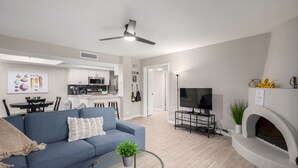 A modern living room with a blue sofa, a glass coffee table, a flat-screen TV, and a fireplace. - Pickleball, 3 pools & hot tubs, gated community, free parking, New listing.  (Phoenix)