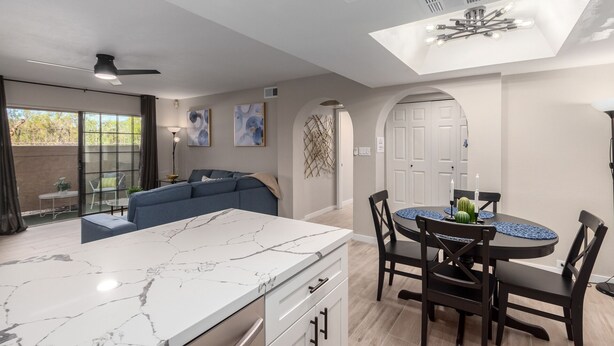 A modern kitchen with a marble countertop, a dining area with a round table and chairs, and a blue sofa in the living area. - Pickleball, 3 pools & hot tubs, gated community, free parking, New listing.  (Phoenix)