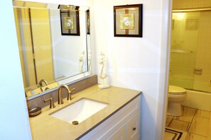 Bathroom features a large mirror, sink, toilet, and shower area with a glass door.