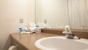 Un bagno d'hotel con lavandino, specchio, porta asciugamani e articoli da toilette.