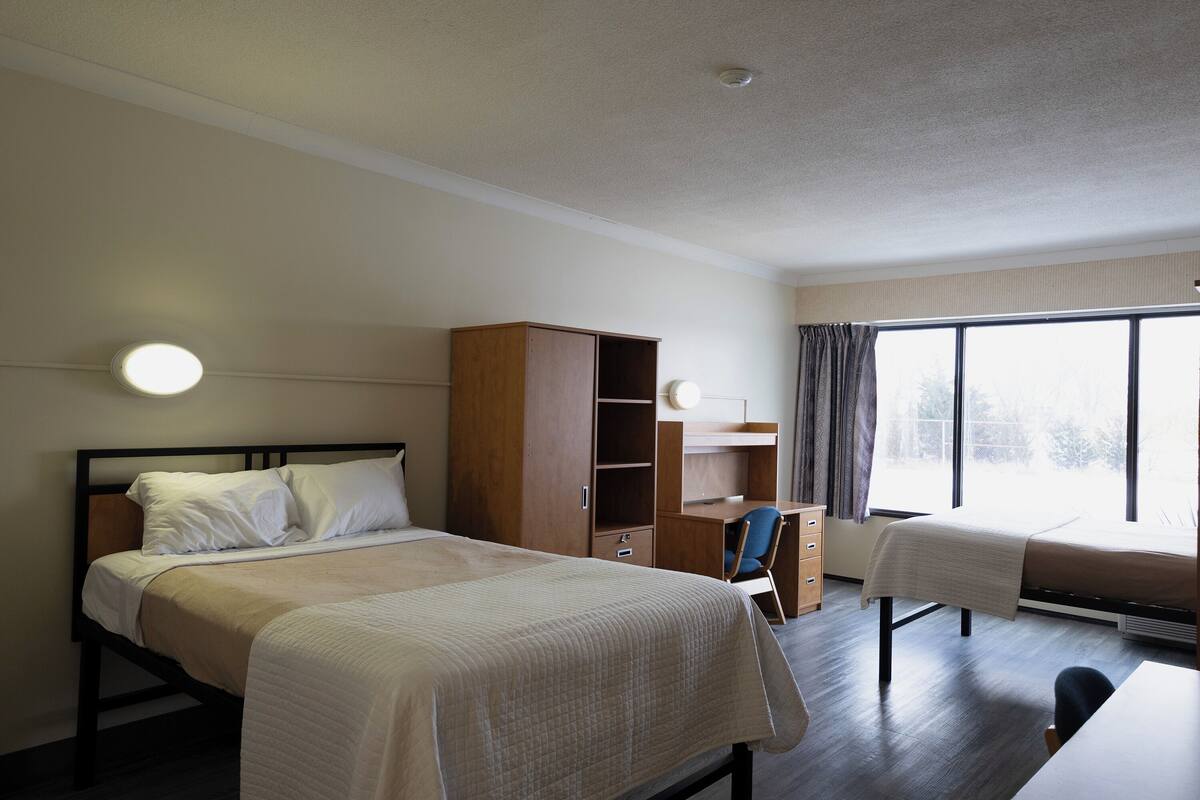 Une chambre d’hôtel comprenant un lit, un bureau, une chaise, une armoire et une fenêtre.