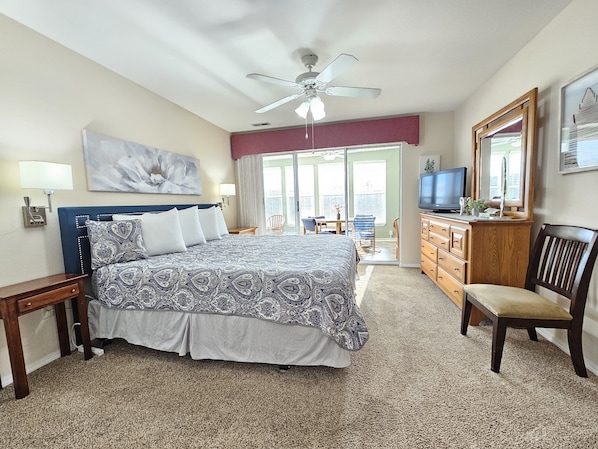 A hotel room with a bed, a dresser, a television, and a balcony with a view.