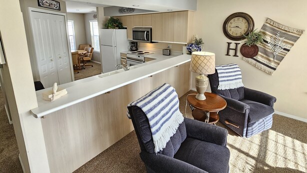 A modern living room with a kitchen area, a sofa, a coffee table, and a wall with a clock and decorative items. - Fairways Oasis Walk-in Suite at the Fairways at Thousand Hills! Great Rates! (Branson)