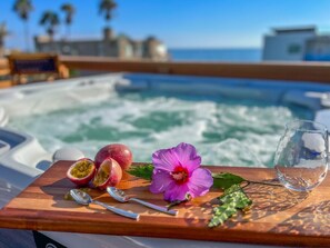 A wooden tray with passion fruit halves, a hibiscus flower, and a glass of water on a boat with a hot tub and ocean view.