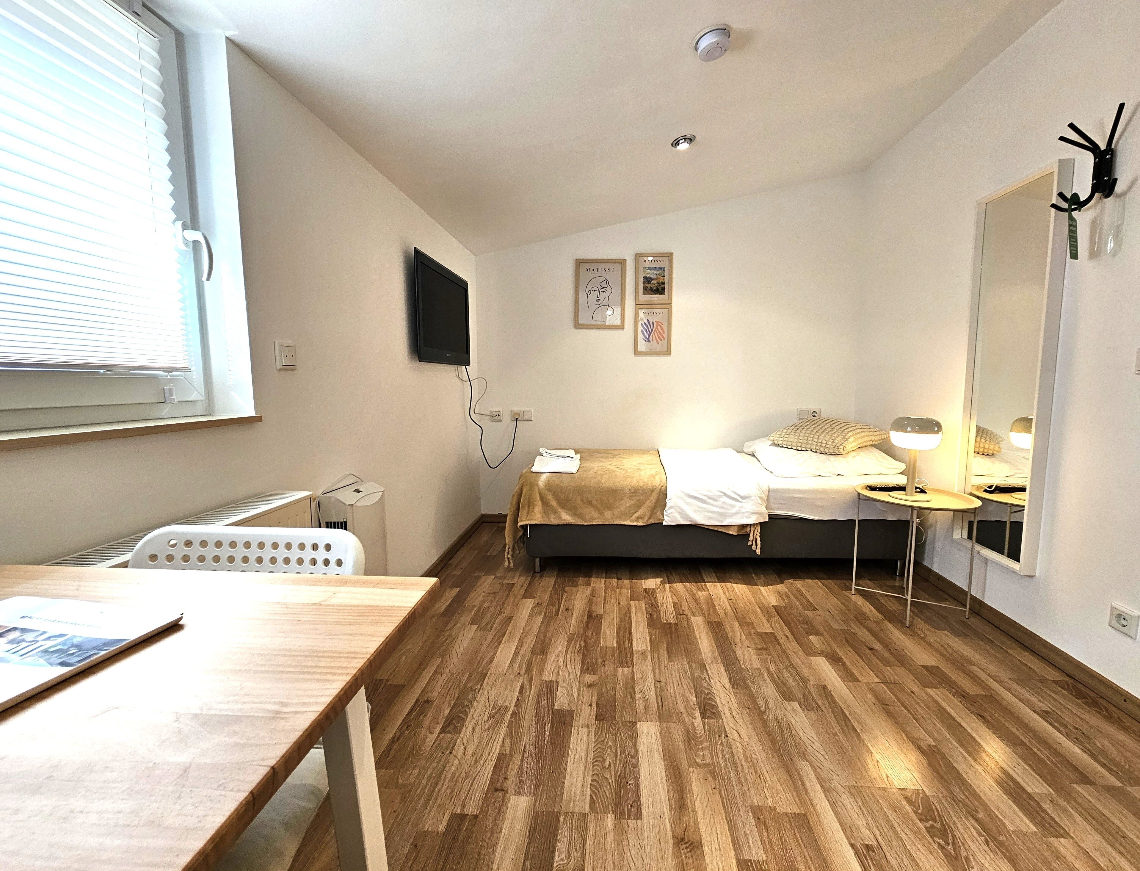 A bedroom with a bed, bedside table, lamp, and a TV mounted on the wall.
