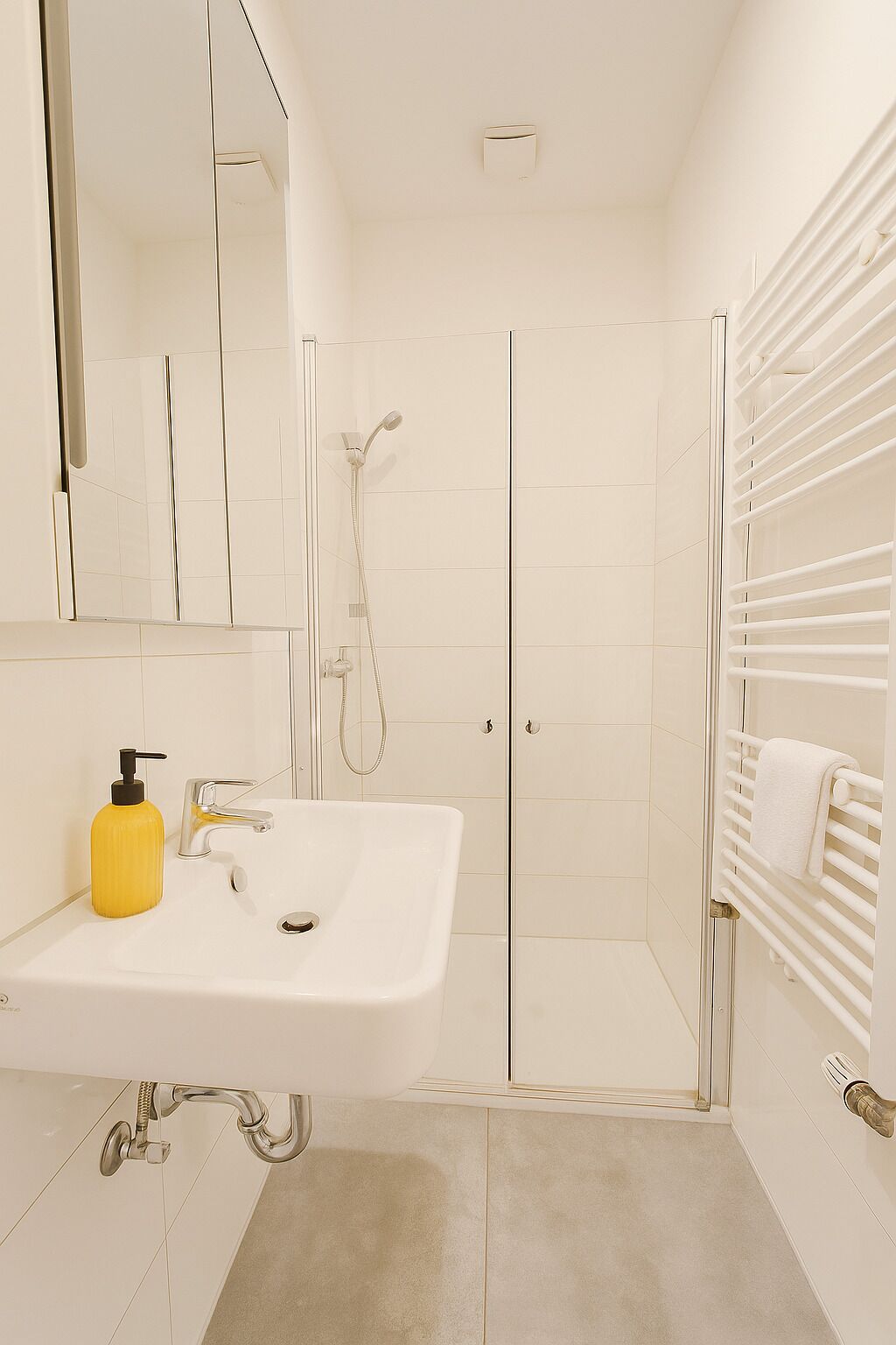 A modern bathroom with a sink, mirror, shower, and towel rack.