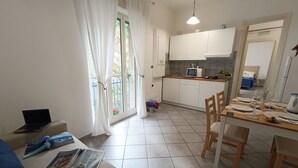 Un salon moderne et bien éclairé, avec un canapé, une table basse sur laquelle sont posés des magazines et un ordinateur portable, ainsi qu’un coin repas avec une table mise pour deux personnes.
