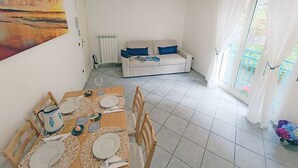 Un coin repas avec une table dressée pour quatre personnes, un radiateur, un canapé avec des coussins bleus et une vue par la fenêtre.
