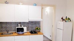 Une cuisine de taille réduite, avec des meubles blancs, un four à micro-ondes, un évier et un réfrigérateur.