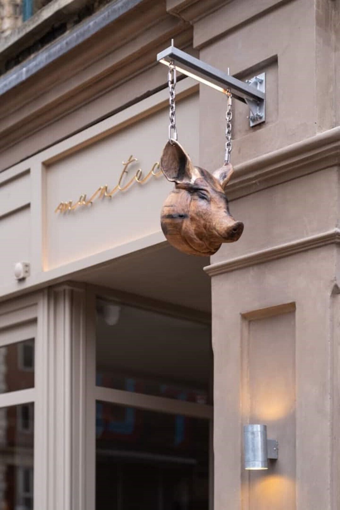 Una escultura de perro colgante frente a un edificio con un letrero que dice 'manteau'.