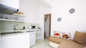 A compact kitchen with a sink, stove, and refrigerator. There is a small dining area with a table and chairs. The room has a neutral color scheme and includes a sofa with decorative pillows. - Hyades - Downtown Suites No 3 , Mykonos Town (Mykonos, Cyclades)