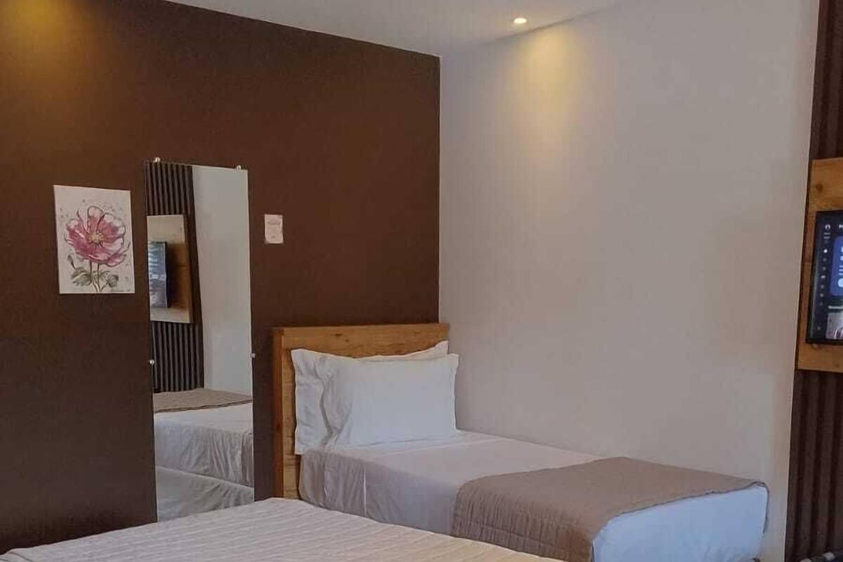 A hotel room with two beds, a wooden headboard, a wall-mounted mirror, and a small shelf with a framed picture.