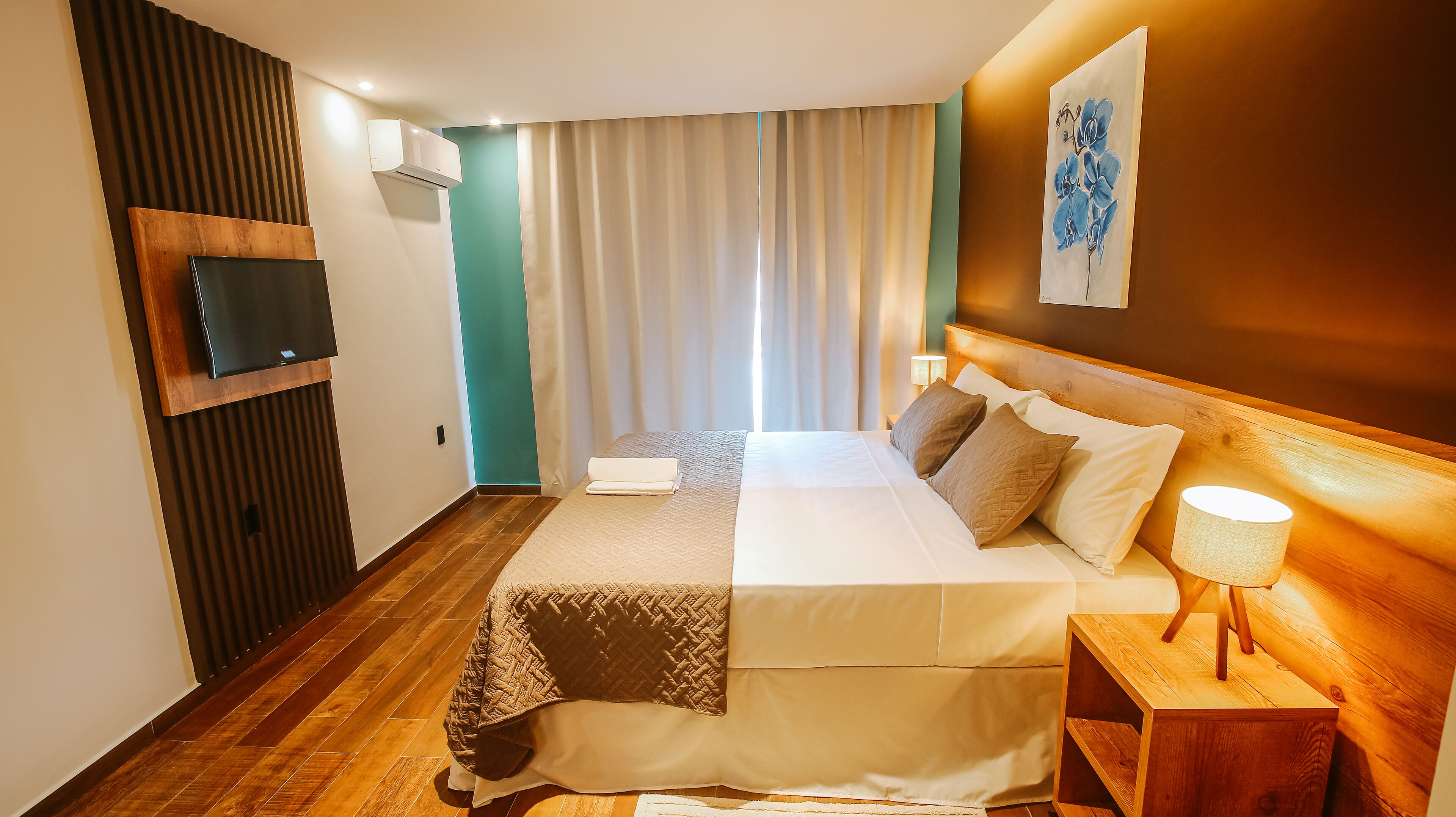 Una habitación de hotel con una cama, televisión, cabecero de madera, mesita de noche y un cuadro en la pared.