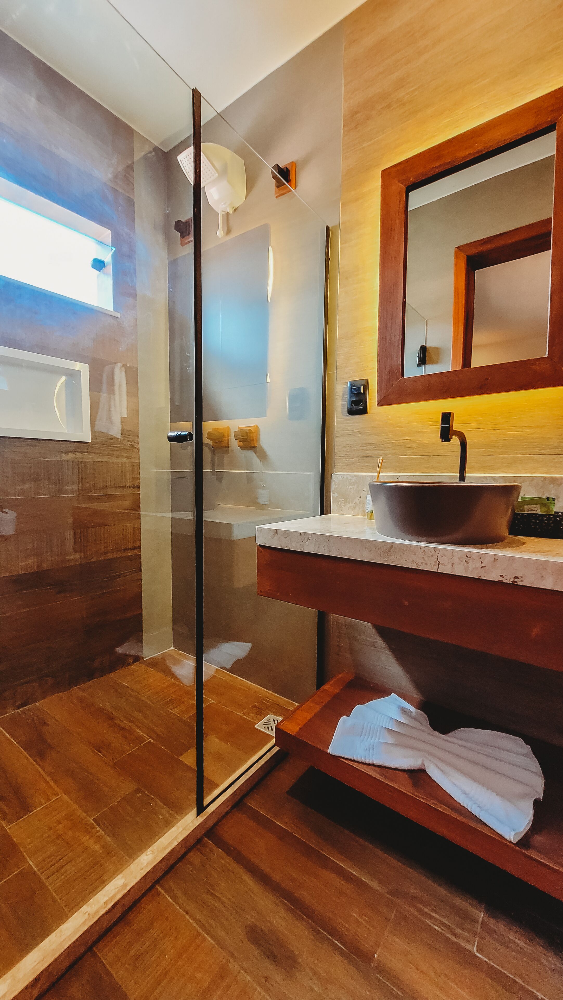 A modern bathroom with a glass shower enclosure, a wooden vanity with a vessel sink, and a large mirror above the sink.