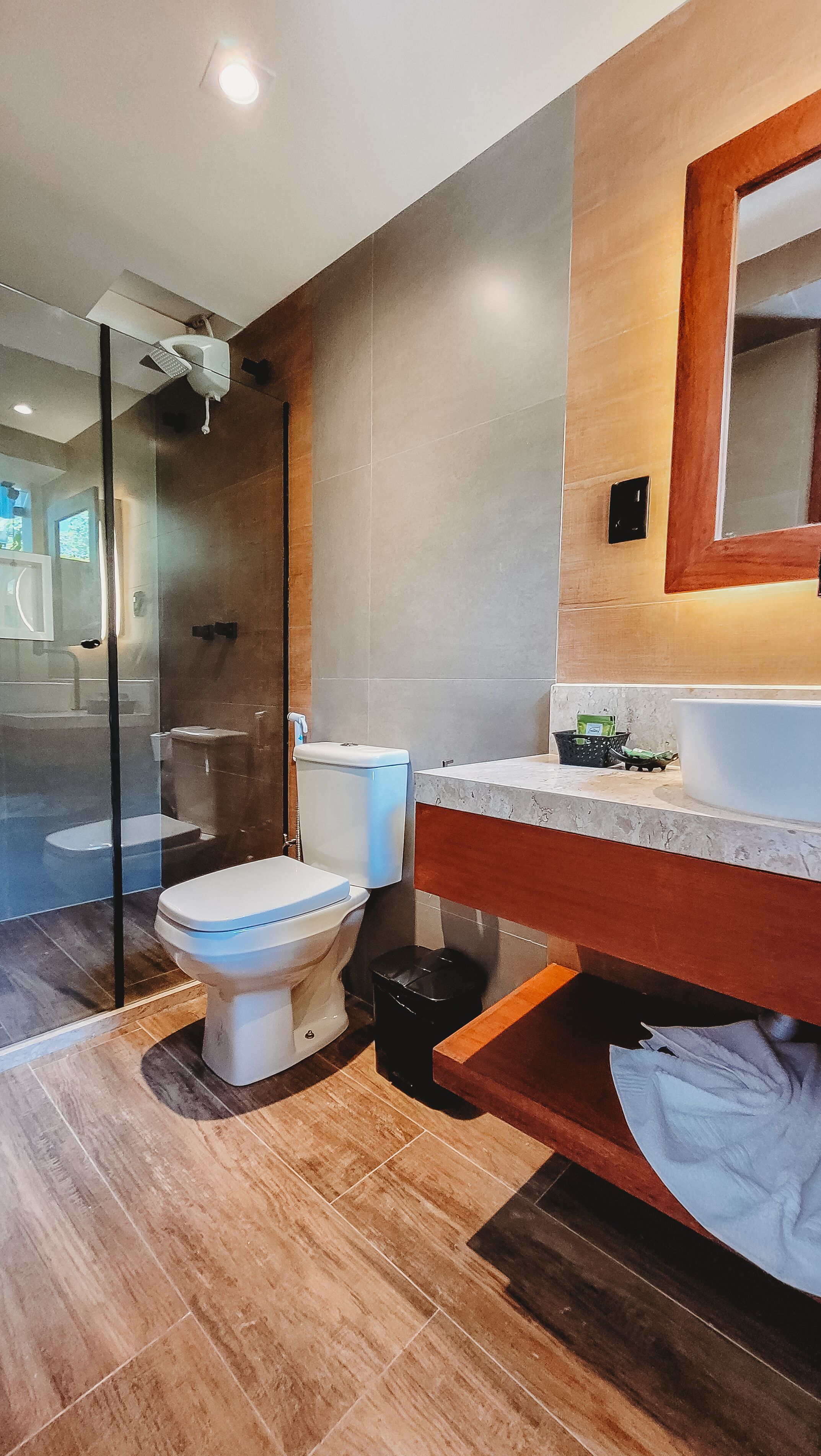 A modern bathroom with a glass shower enclosure, a toilet, and a sink with a wooden vanity.