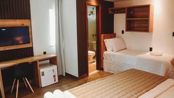 A hotel room with a bed, a desk with a TV, a small fridge, and a wooden shelf.