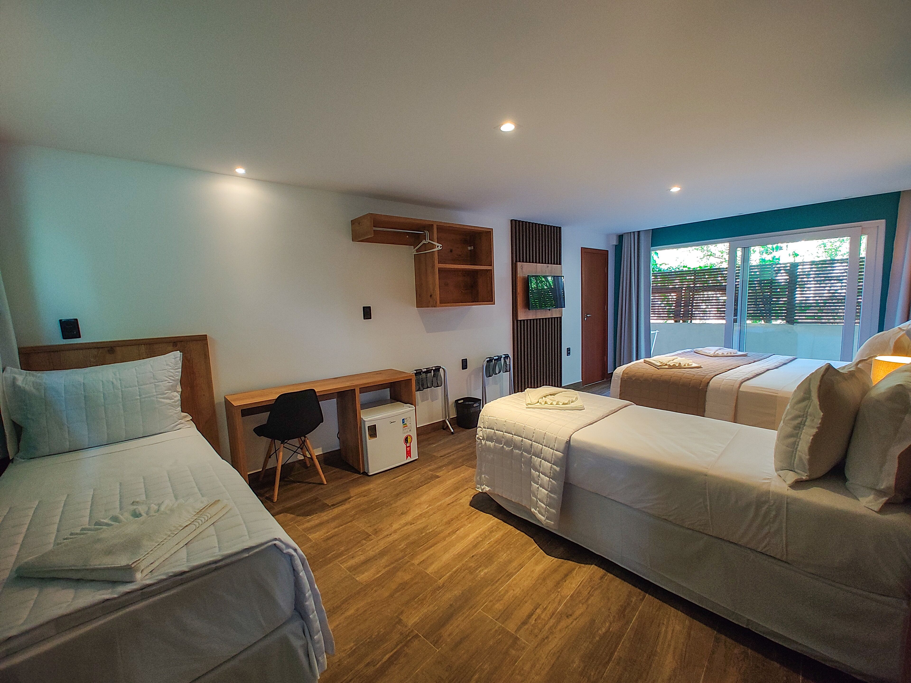 A hotel room with two beds, a desk, a small refrigerator, and a TV.