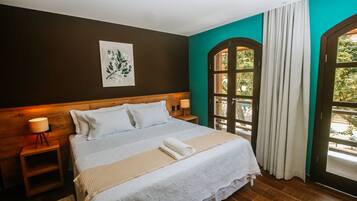 A neatly made bed with white linens and a beige throw blanket, a wooden headboard, a bedside table with a lamp, and a window with curtains.