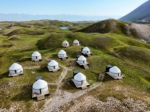 Une série de yourtes blanches disposées sur une colline verdoyante, offrant une vue dégagée sur les montagnes lointaines.