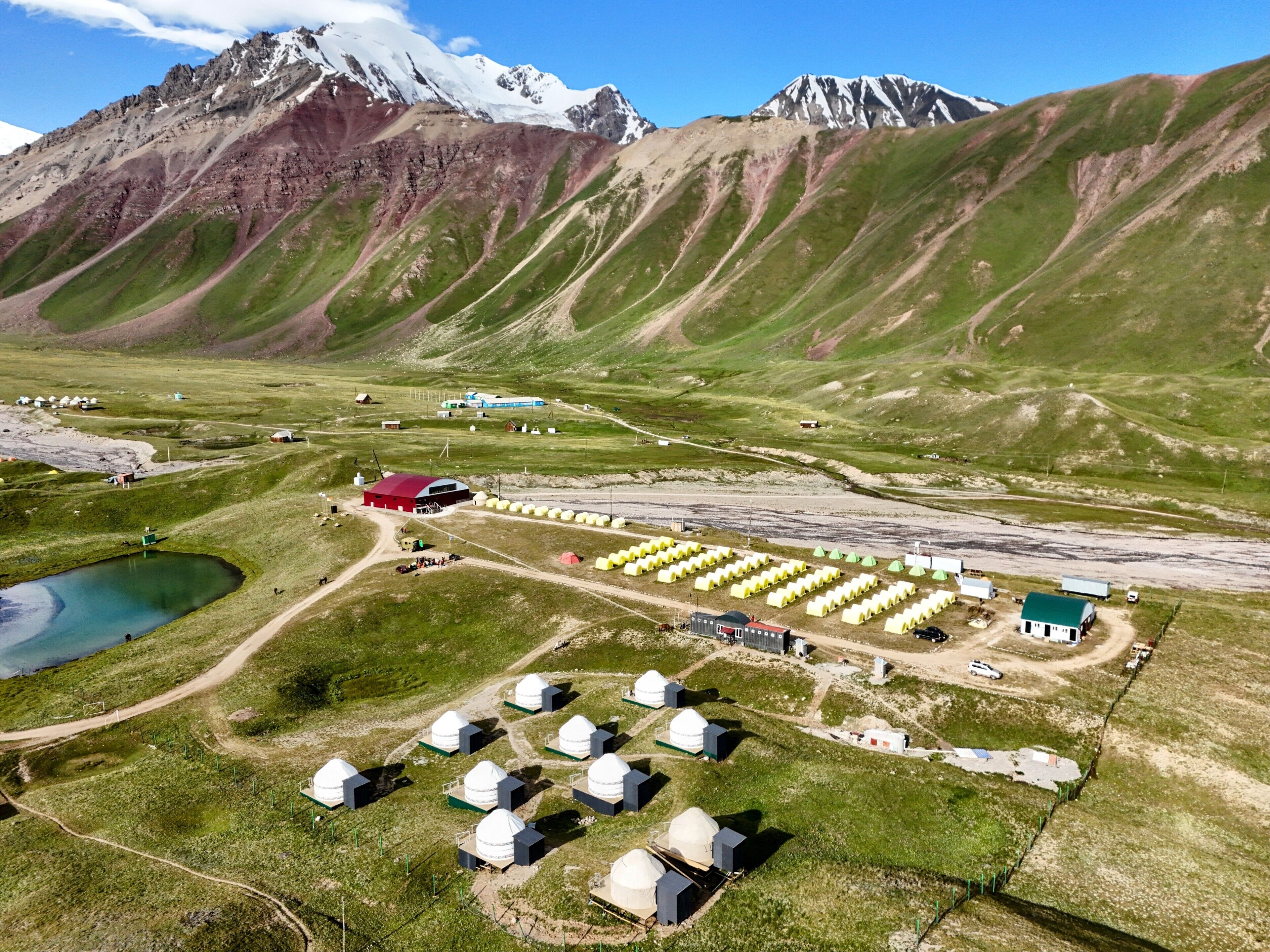 Une région montagneuse isolée, avec un petit village comprenant plusieurs bâtiments blancs en forme de dôme, un bâtiment rouge et un lac.