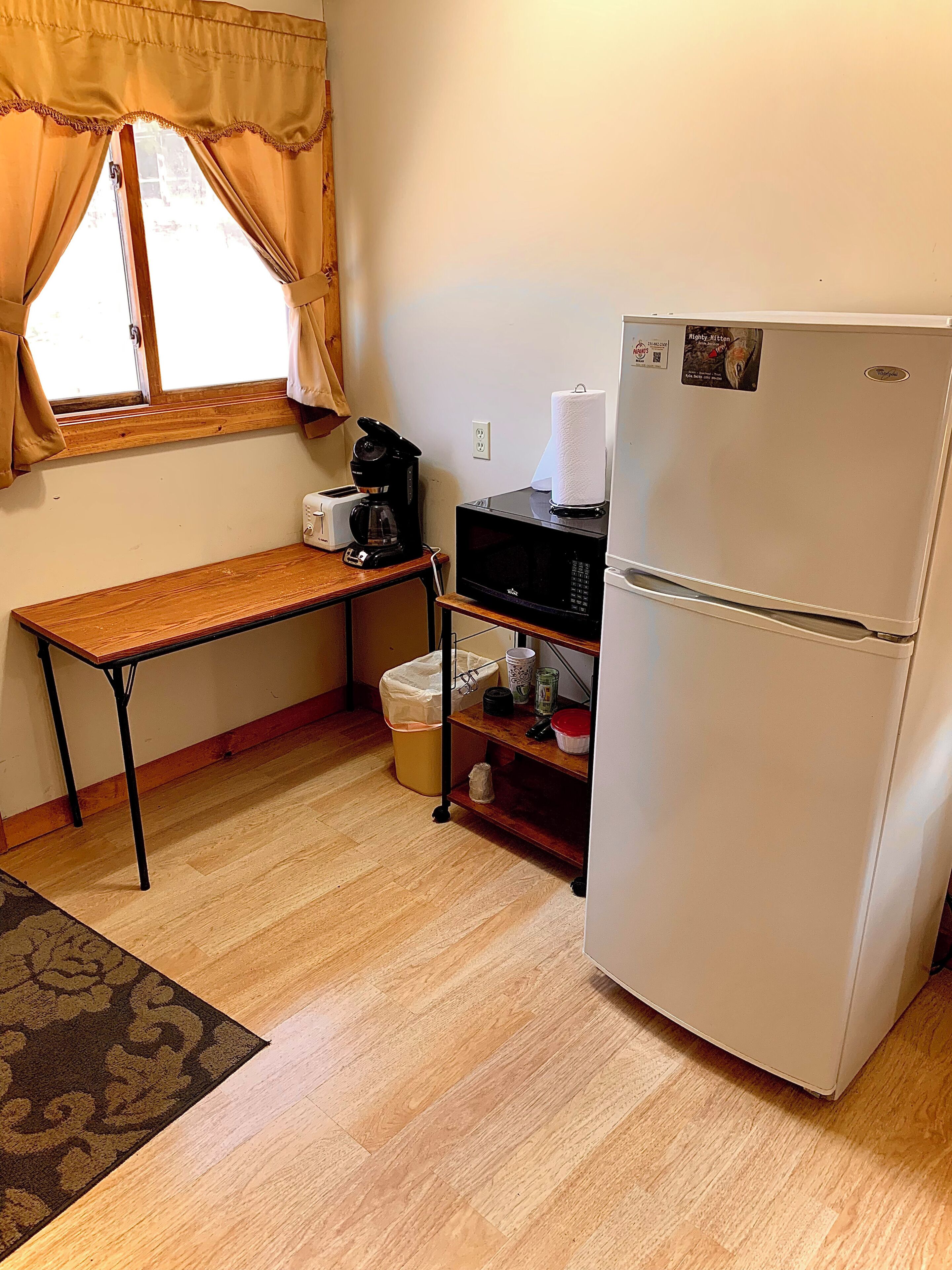 Cocina compacta con refrigerador, microondas, tostadora y cafetera sobre una mesa de madera.