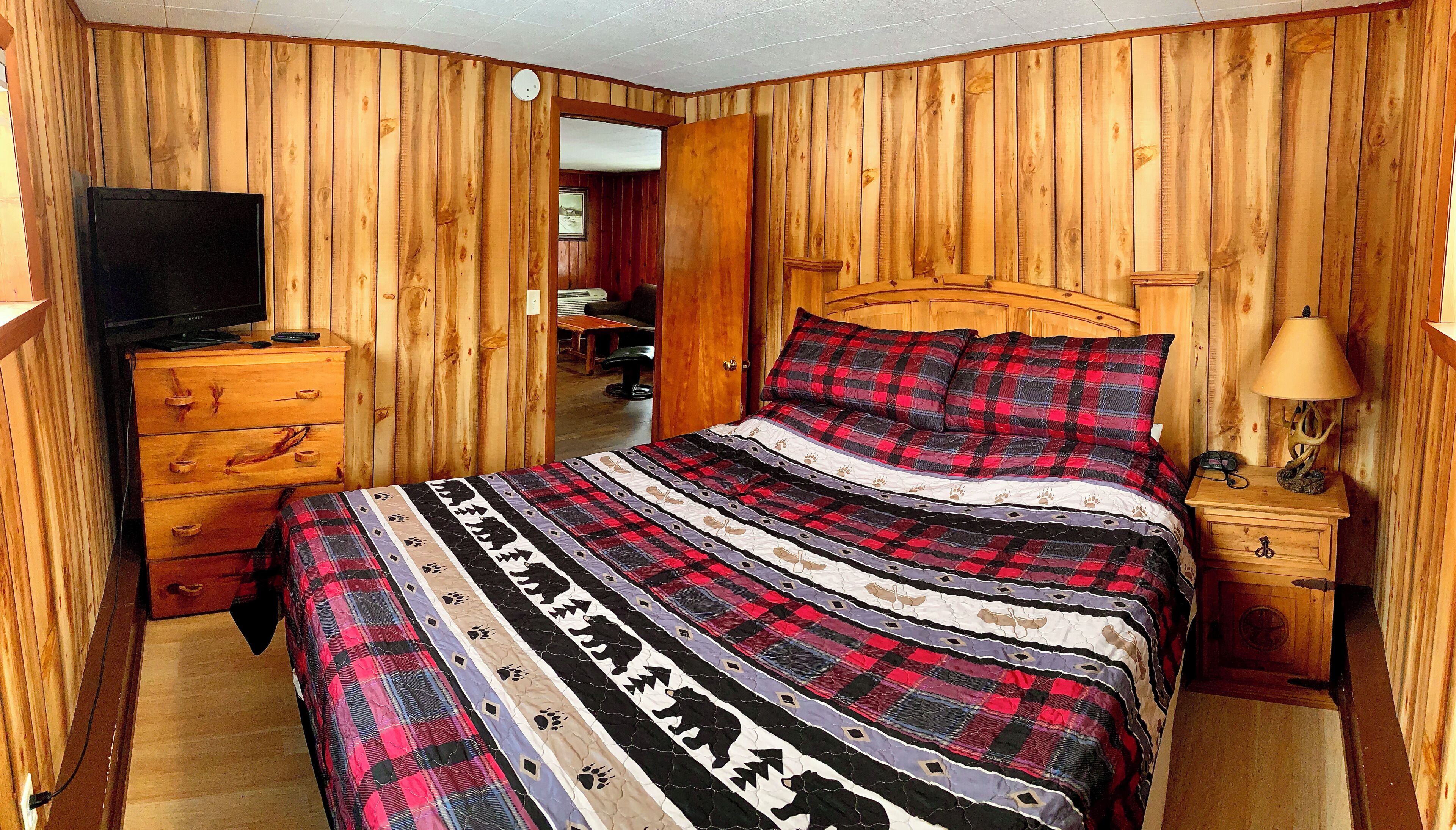 A wooden-paneled room with a bed, dresser, TV, and lamp.