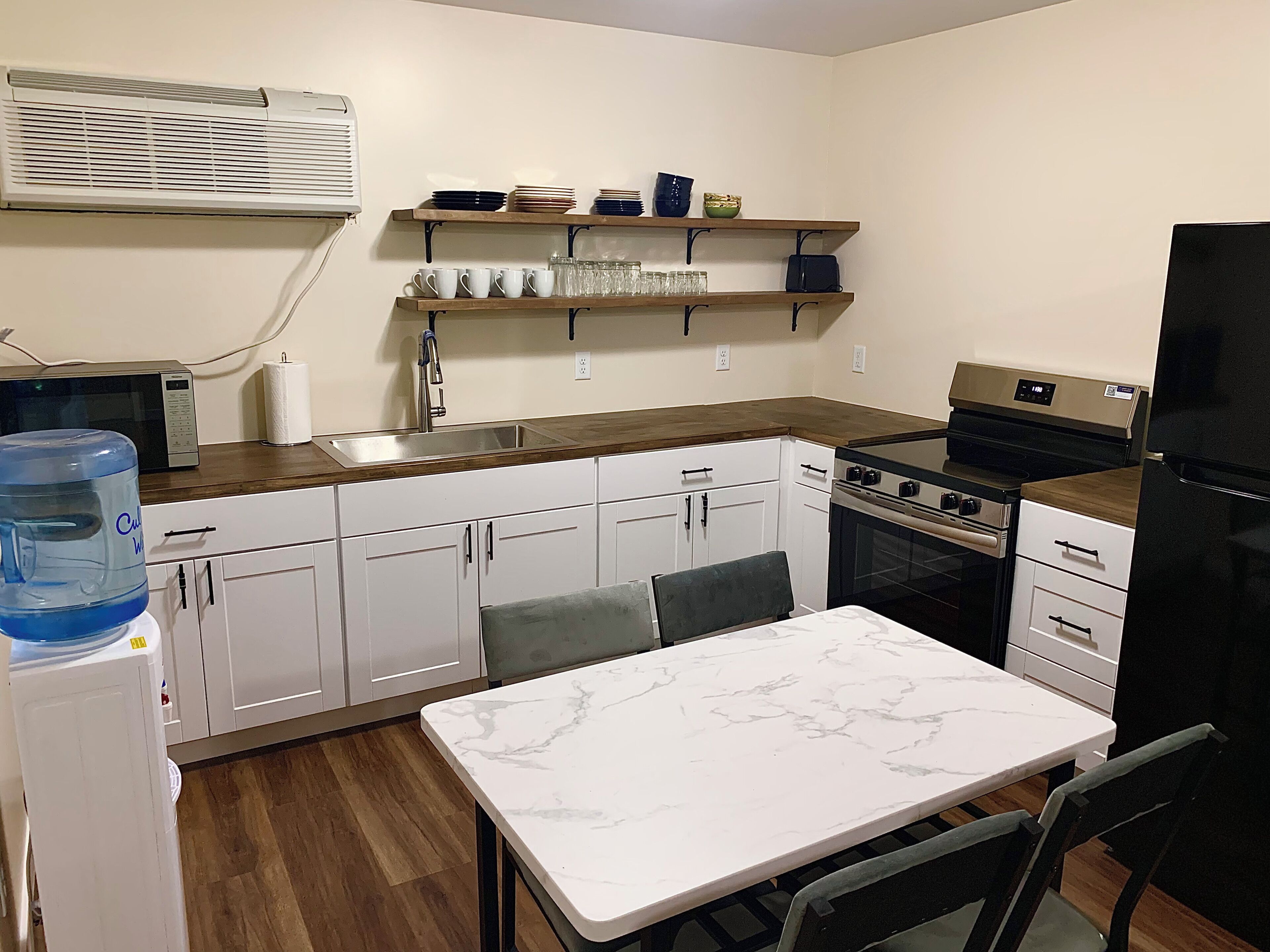 Uma cozinha compacta com armários brancos, forno embutido, micro-ondas e um bebedouro.