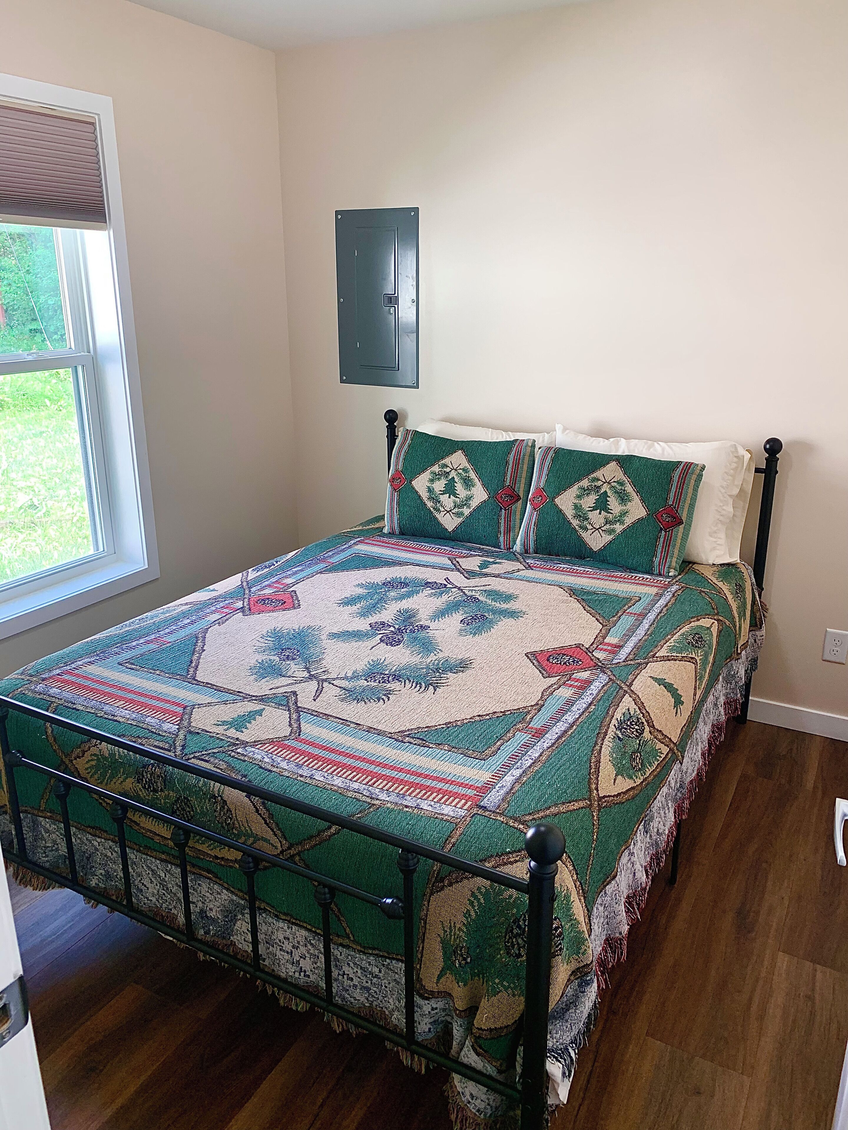 A bed with a patterned bedspread, a headboard, and a window with blinds.