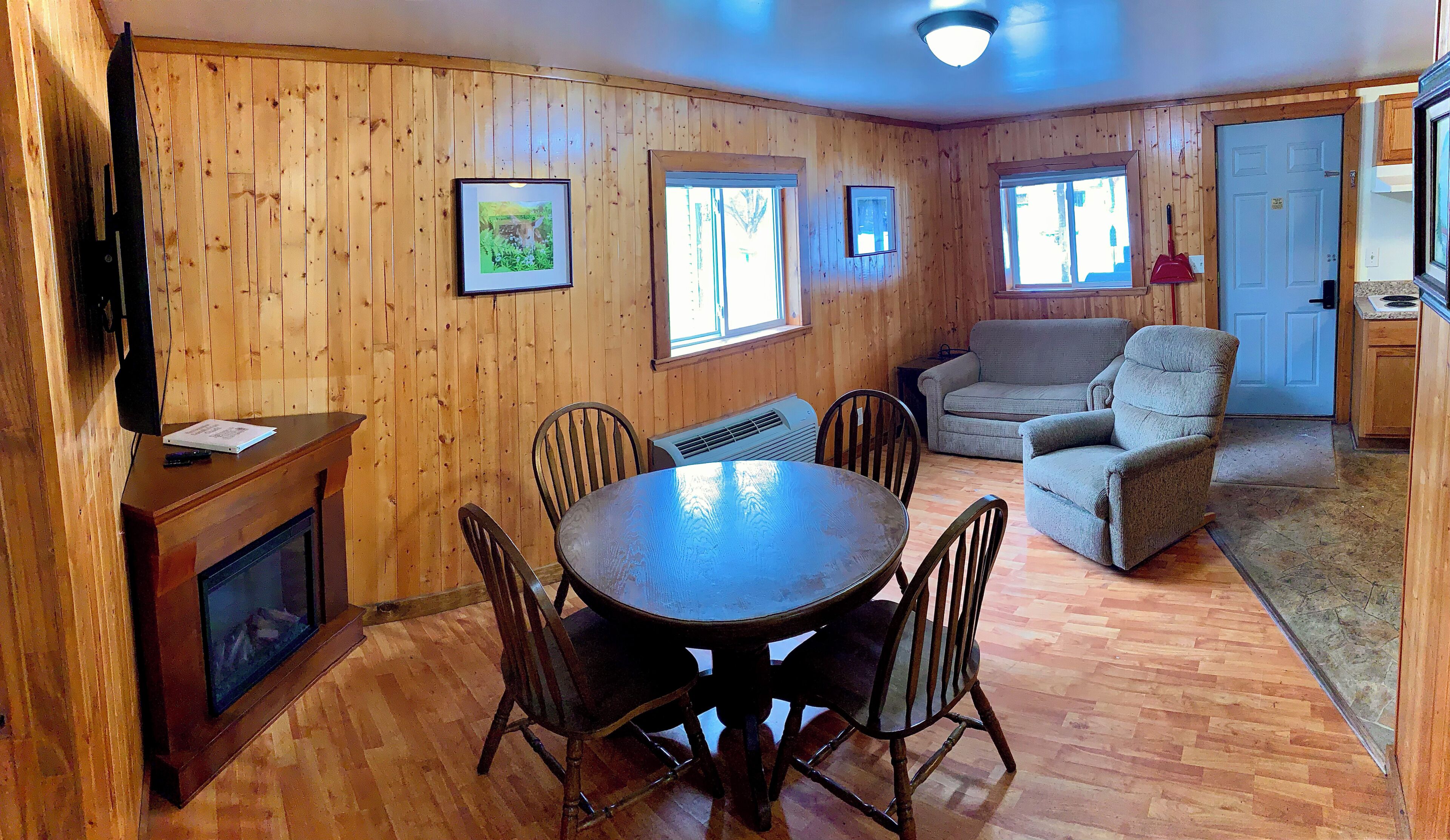 A wooden-paneled room with a dining table, chairs, a sofa, and a television.