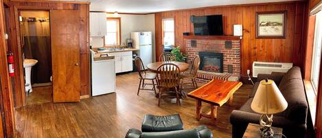 A wooden interior with a dining table, chairs, a sofa, a fireplace, and a kitchen area.