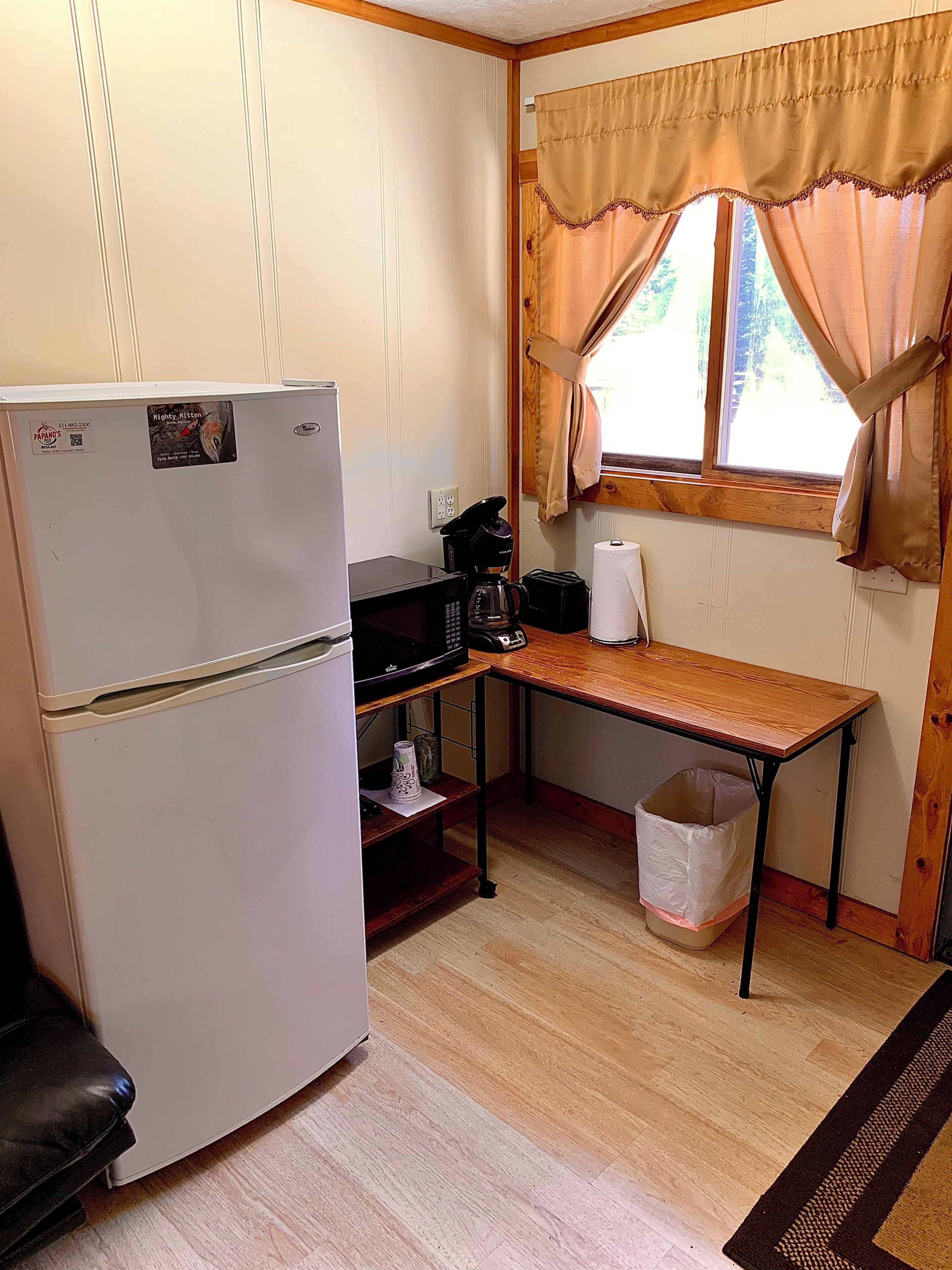 A compact kitchen with a refrigerator, coffee maker, and a small trash bin.