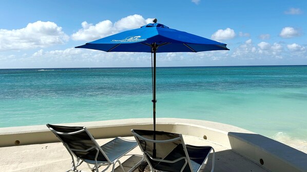 A boat with two chairs and a blue umbrella, overlooking turquoise ocean water.