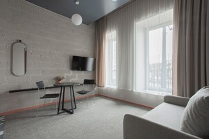 Een moderne kamer met een bakstenen muur, een flatscreen televisie, een ronde eettafel met stoelen, een bank en grote ramen met gordijnen.