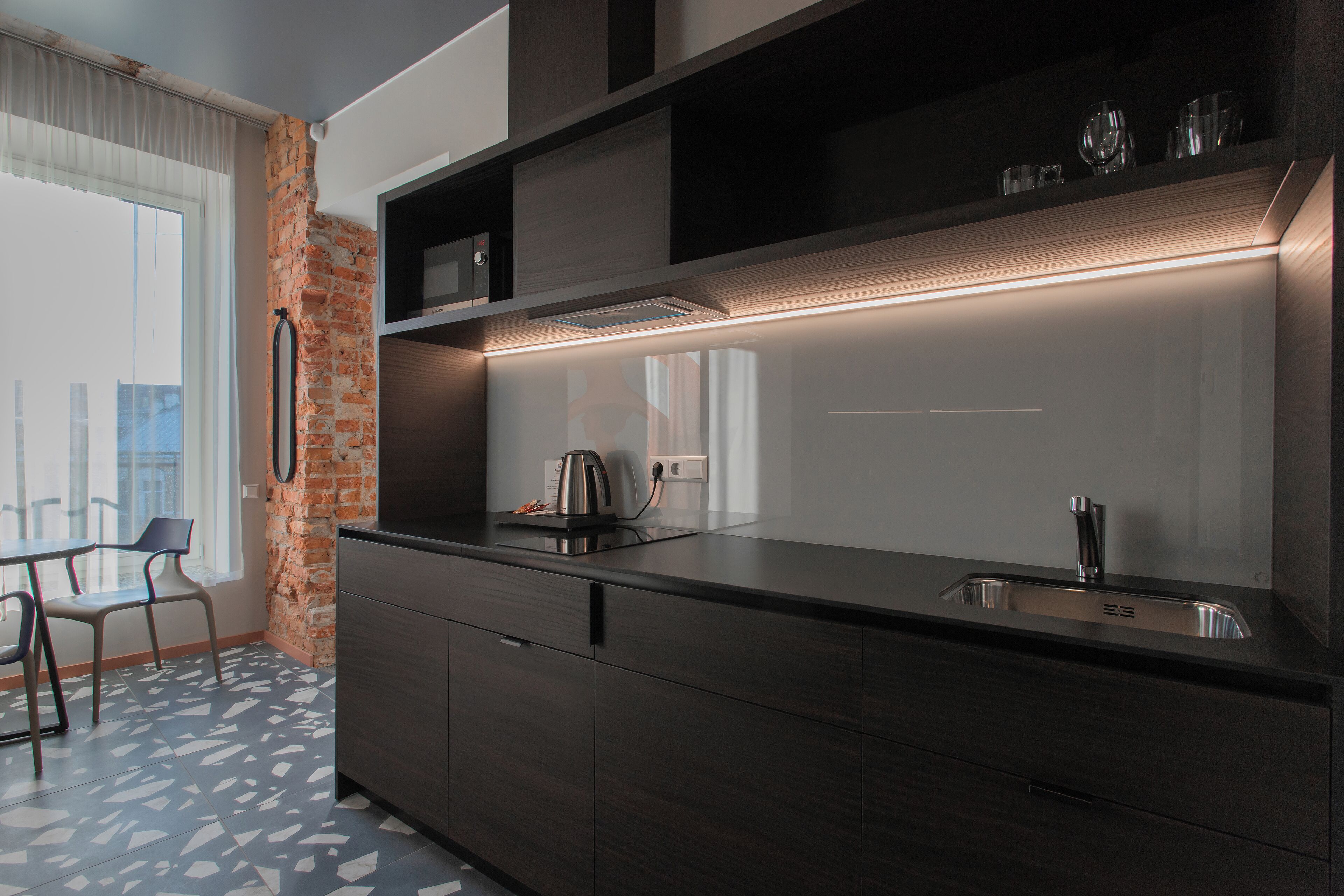 Una cocina moderna con armarios oscuros, microondas integrado y un lavamanos de acero inoxidable.