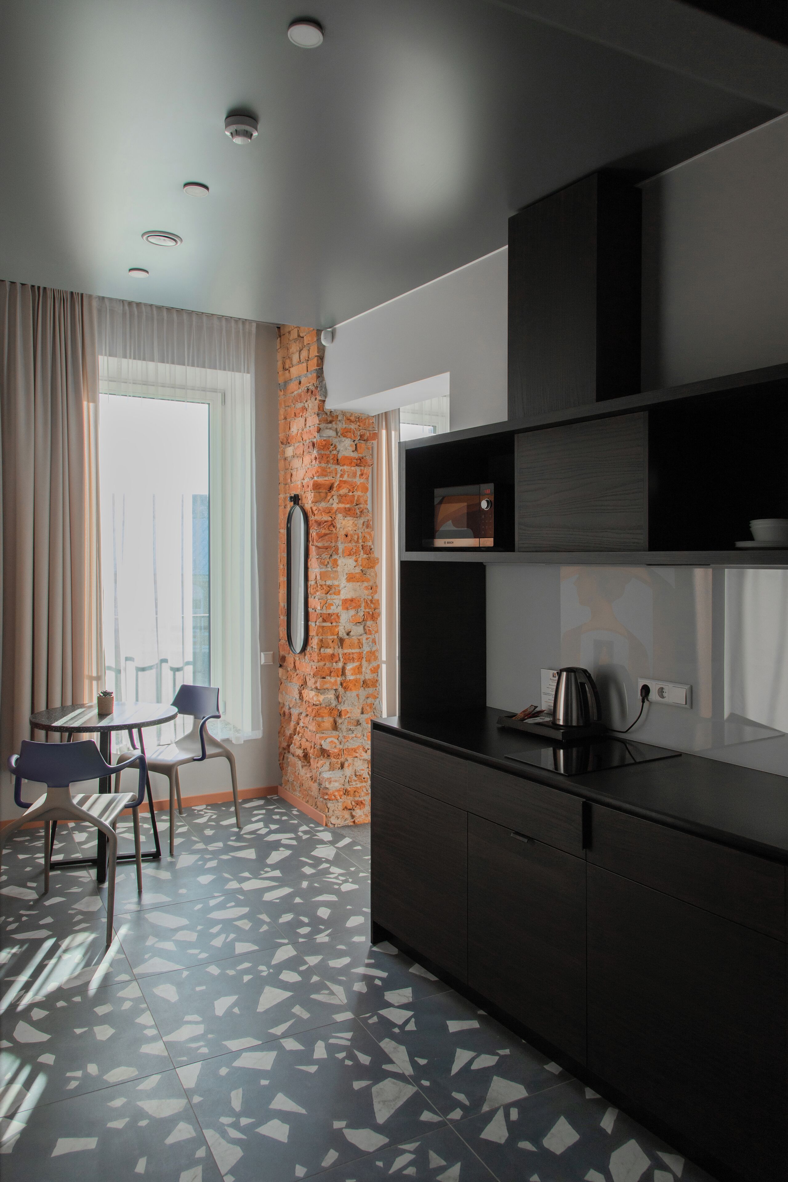 A modern kitchen with a brick accent wall, a dining area with chairs, and a patterned floor.