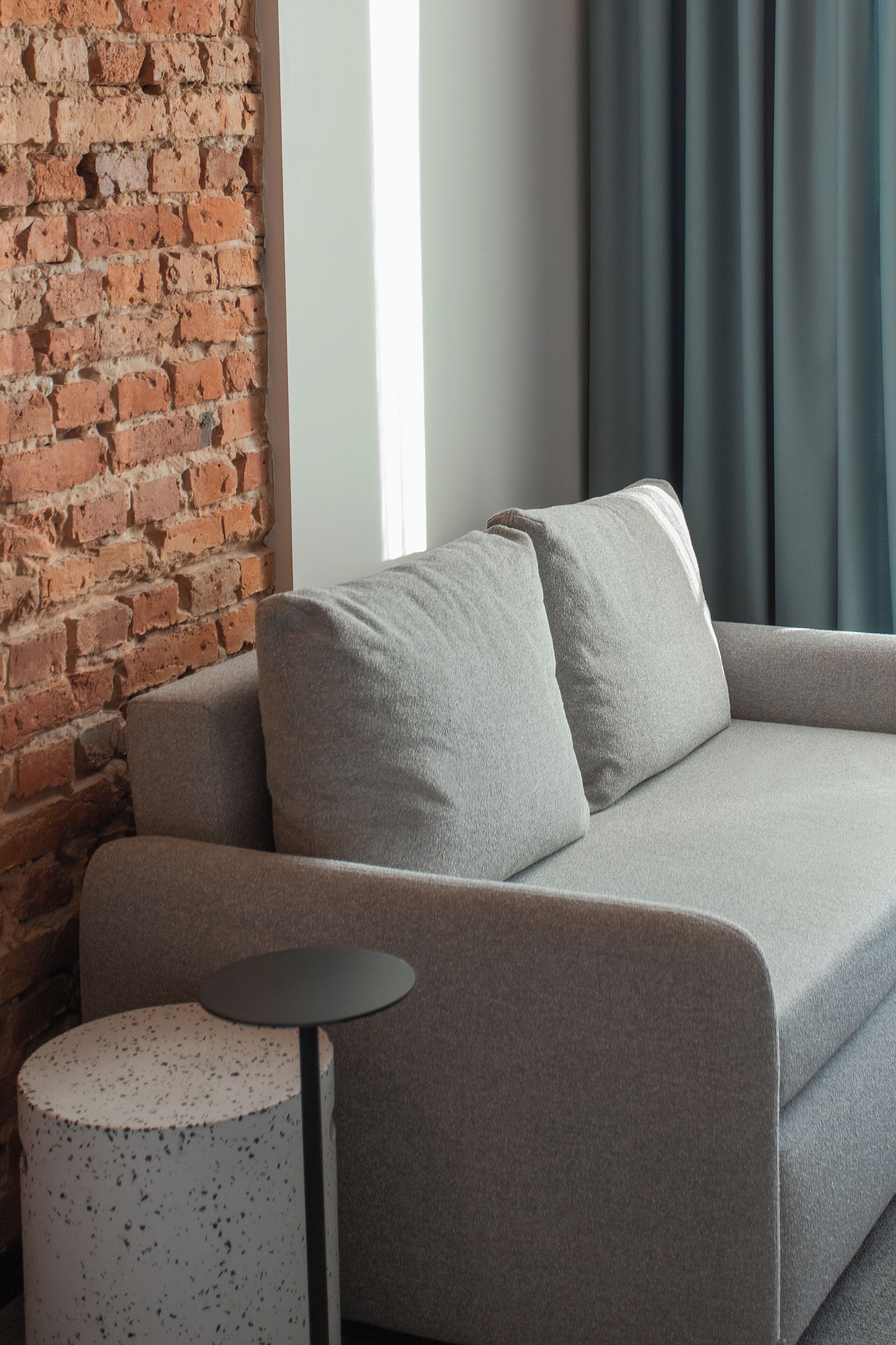 A modern living room with a brick wall, a grey sofa, and a small round table.
