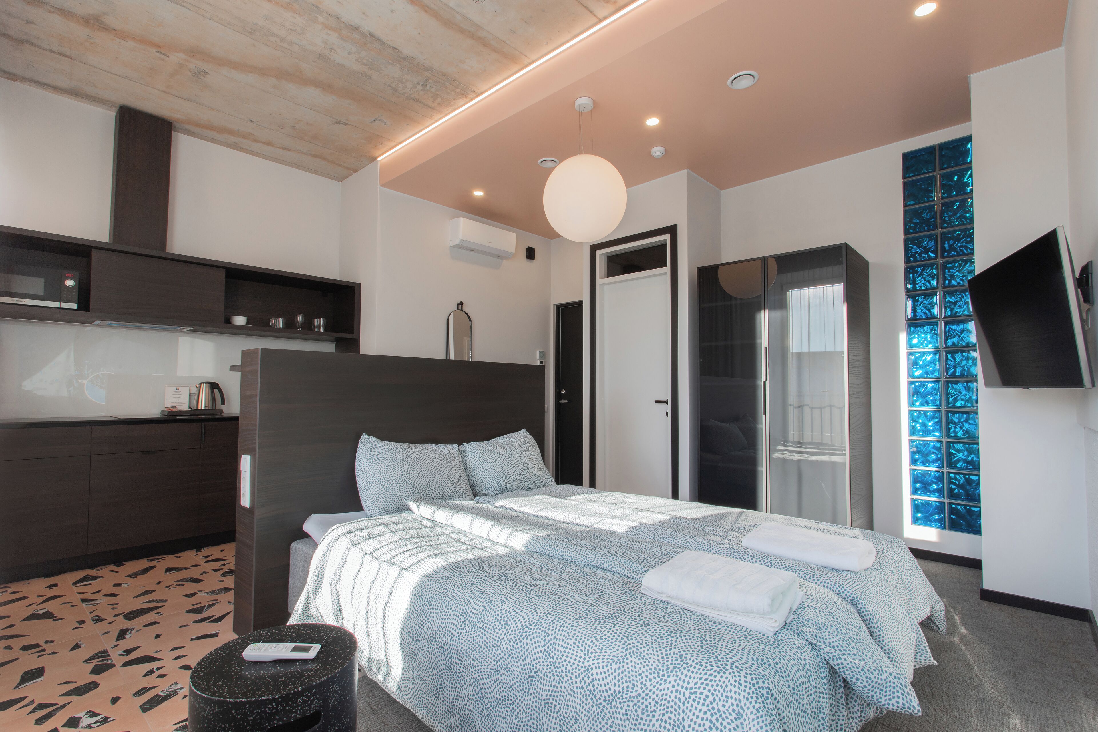 A modern hotel room with a large bed, a built-in wardrobe, a small seating area, and a TV mounted on the wall.