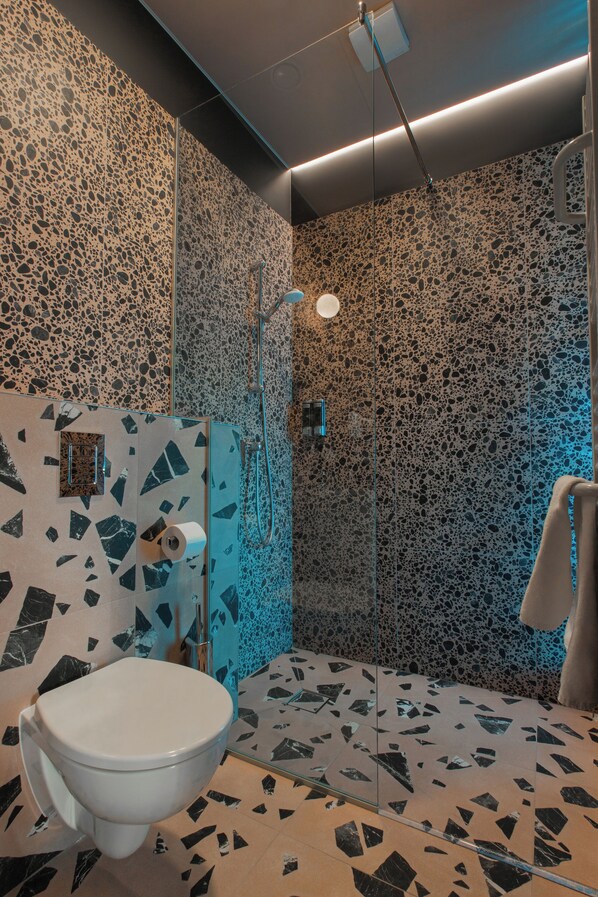 Un baño de diseño moderno con inodoro, ducha envuelta en vidrio y pared con estampado de mármol.