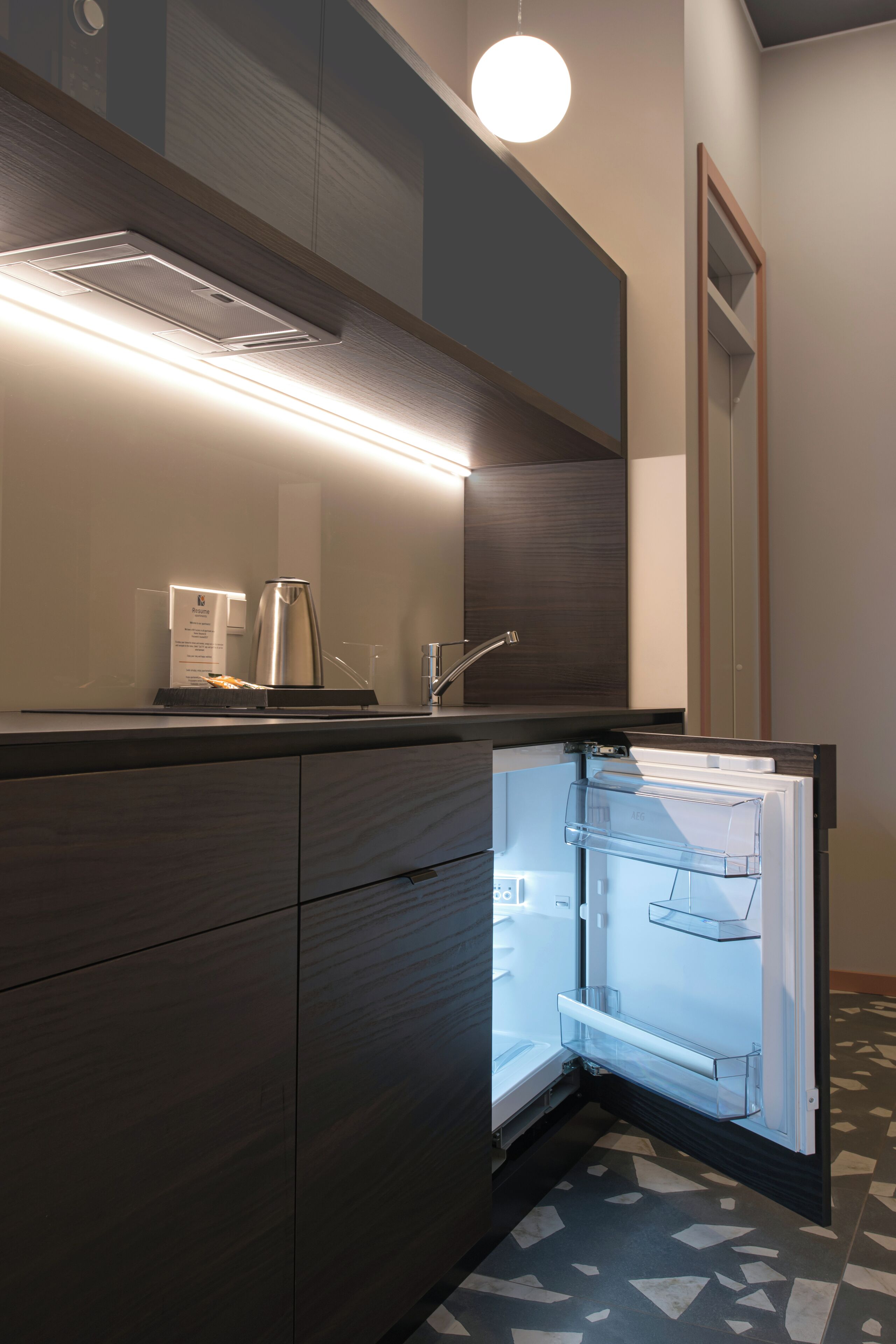 Una cocina moderna con un refrigerador empotrado, una cafetera y una lámpara sobre la encimera.