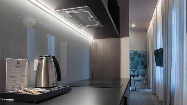 A modern kitchen with a stainless steel kettle, a coffee maker, and a tray of pastries. - Resume Apartments (Kaunas)