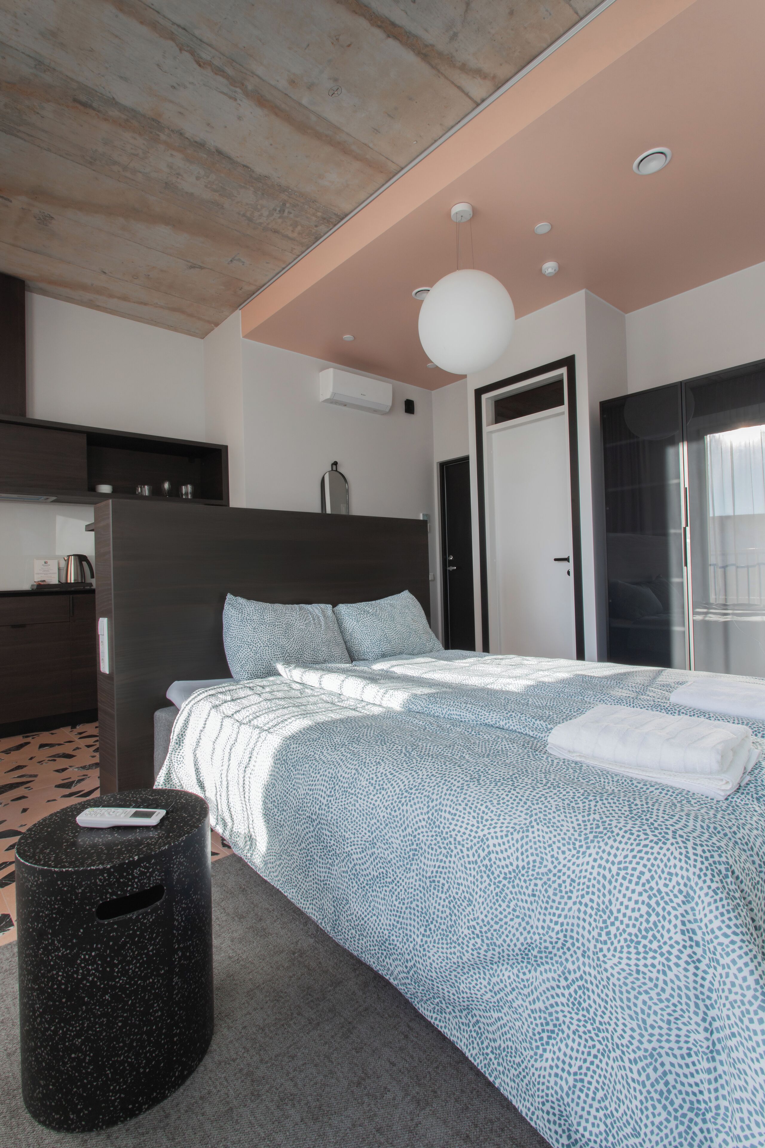 Een moderne slaapkamer met een groot bed, een houten plafond, een zwart poufje en een badkamer met een glazen deur.